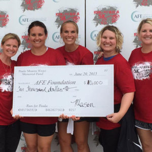 A group of women holding a large check from a memorial fund at 5K event.