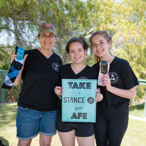 Three young women holding a sign that reads take a stance against AFE.