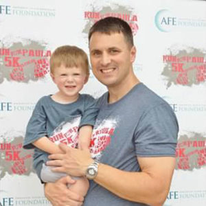 AFE widower holding his toddler son at a 5K event.