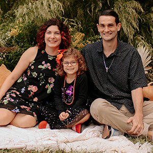 Emily with her husband and daughter sitting on a picnic blanket.